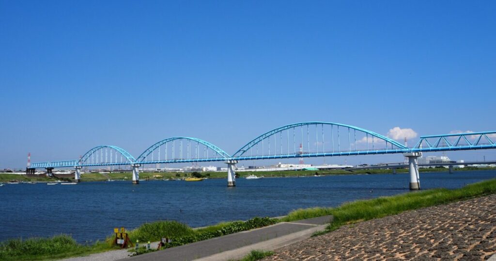 青いアーチ橋が川を横断する開放的なリバーサイド風景