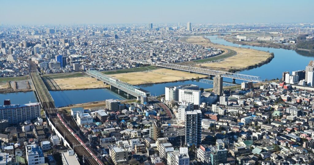 鉄道橋と道路橋が交差する川沿いの市街地を俯瞰した景色