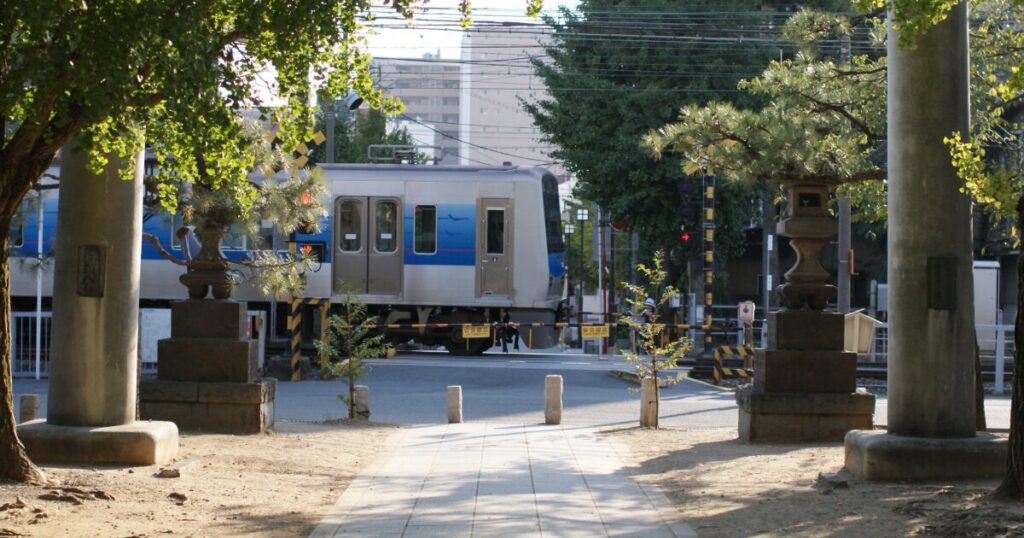 神社の参道越しに踏切を通過する電車のある風景