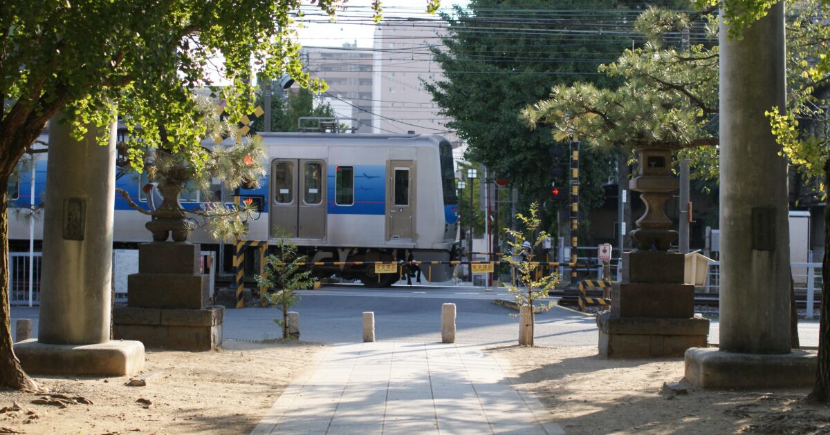 神社の参道越しに踏切を通過する電車のある風景