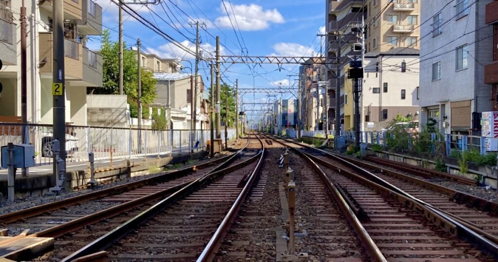 住宅街の中を走る線路と電線が続くローカル鉄道の風景