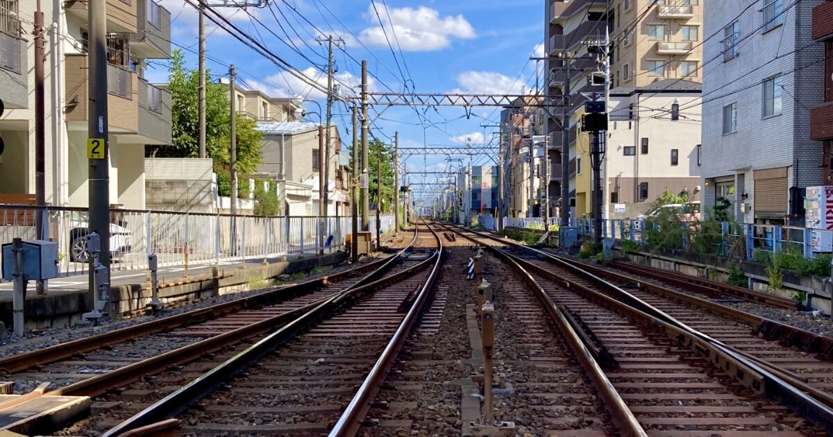 住宅街の中を走る線路と電線が続くローカル鉄道の風景