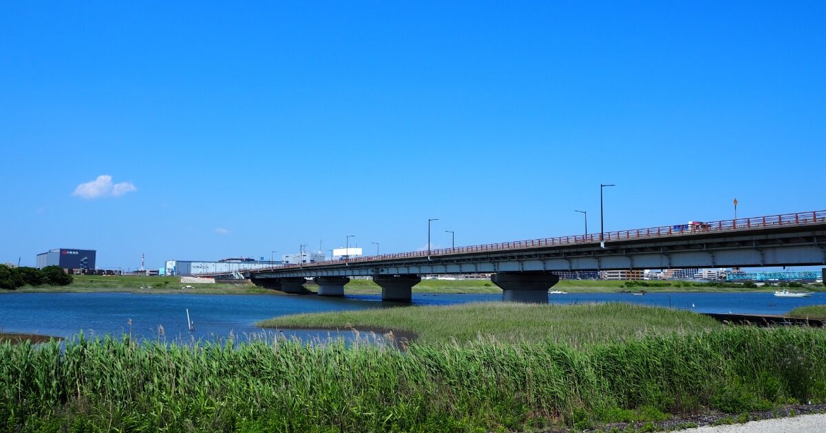 青空の下で川に架かる橋と草地が広がる開放的な風景